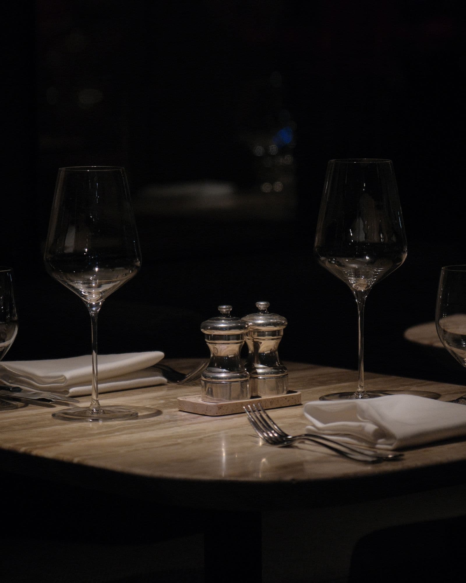 A dimly lit fine dining table set with wine glasses and white linen napkins